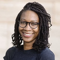 Akua Nyame-Mensah ACC headshot photo, smiling woman with dark hair wearing glasses and a dark top in front of beige background