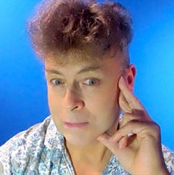 Andrew Shaffer MCC headshot photo, man in front of blue background with left hand on face
