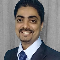 Arvind Ramasundaram PCC headshot photo, smiling man with dark hair and facial hair in suit and tie against light gray background