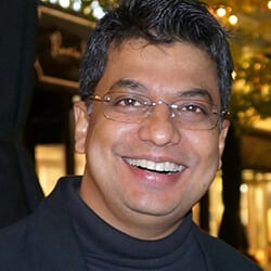 Sadhan Bhattacharya headshot photo, smiling man with dark hair wearing glasses and black top