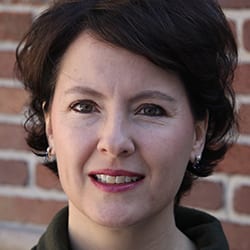 Dr. Carrie Arnold PCC headshot photo, smiling woman with short dark hair in front of a brick wall