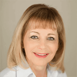 Daniel Grant MA PCC FHEA FRSA headshot photo, smiling woman with blond hair wearing a white collared shirt in front of tan background