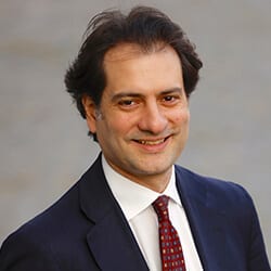 Danilo Schipani headshot photo, smiling man with dark hair wearing dark blazer white collared shirt and red tie in front of neutral background