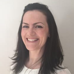 Naimh Gaffney PMC ACC headshot photo, smiling woman with dark hair wearing a white top in front of white wall