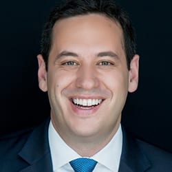 Gideon Culman PCC MCC headshot photo, smiling man in suit and blue tie in front of black background