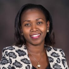 Emily Kamunde-Osoro ACC headshot photo, smiling woman with dark hair and patterned blazer in front of dark background