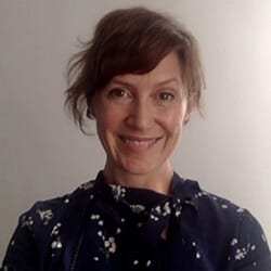Janine Hopkinson PCC headshot photo, smiling woman with brown hair and a dark top in front of a white wall