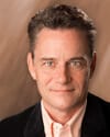 Jeff Hull headshot photo, smiling man wearing black blazer and light button up shirt in front of neutral background