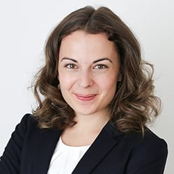 Judith Blank ACC headshot photo, smiling woman with curly brown hair wearing a black blazer and white top