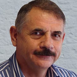 Leon Steyn headshot photo, smiling man wearing striped collared shirt in front of wall