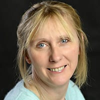 Penny Gundry headshot photo, smiling blond woman with light top in front of black background