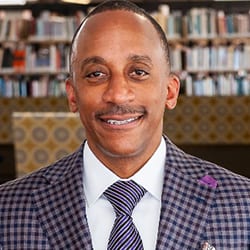 Peter A James ACC PCC headshot photo, smiling man wearing patterned blazer and tie in front of a bookcase