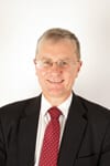 Peter Black headshot photo, smiling man wearing a suit red tie and glasses in front of a white wall