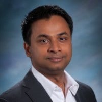 Rajat Garg MCC headshot photo, smiling man with dark hair wearing a dark suit white collared shirt and sitting in front of a neutral background