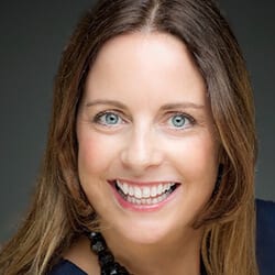 Regina Cook headshot photo, smiling woman with brown hair wearing a dark necklace and top in front of a gray background