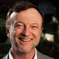 Sam Magill MCC headshot photo, smiling man with dark hair in front of a dark background