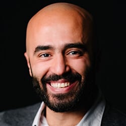 Samer Hassan MCC headshot photo, smiling man with dark suit in front of black background