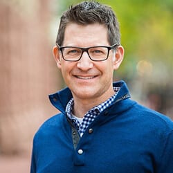Sal Silverster headshot photo, smiling man with dark hair wearing glasses and blue sweater outside