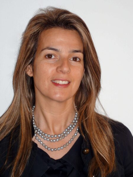 Silvia Viola PCC headshot photo, smiling woman with brown hair wearing black top standing against white wall