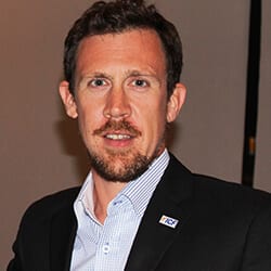 Matt Trenchard headshot photo, man with dark hair wearing suit and striped collared shirt