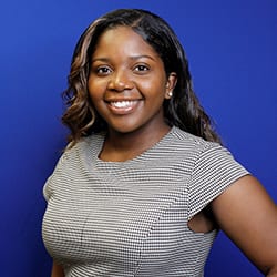 Tyler Parker headshot photo, smiling woman in stripped dress in front of blue background