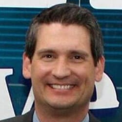 Dr. Brian Underhill PCC headshot photo, smiling man in suit in front of white and blue background