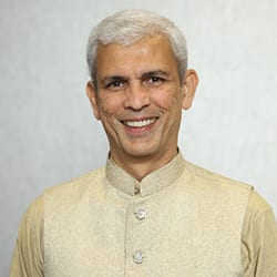 Venkatesh Madurai Subramanian headshot photo, smiling man with white hair and light yellow clothing standing in front of a light background