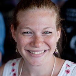 Whitney Hess PCC headshot photo, woman smiling wearing a white top with flowers in front of a dark background