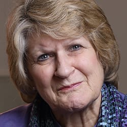 Alison Hodge headshot photo, smiling woman with blond hair purple top and blue scarf in front of tan background