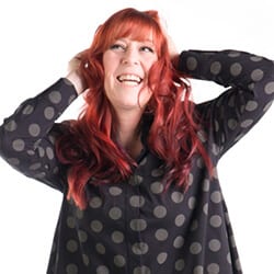 Feroshia Knight MA MCC headshot photo, smiling woman with red hair wearing black and gray patterned top in front of white background