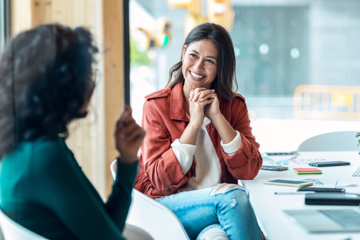 Two women having a focused discussion at a table with a laptop open in front of them.