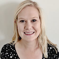 Savannah Patton headshot photo, smiling blond woman wearing black and white top in front of white wall