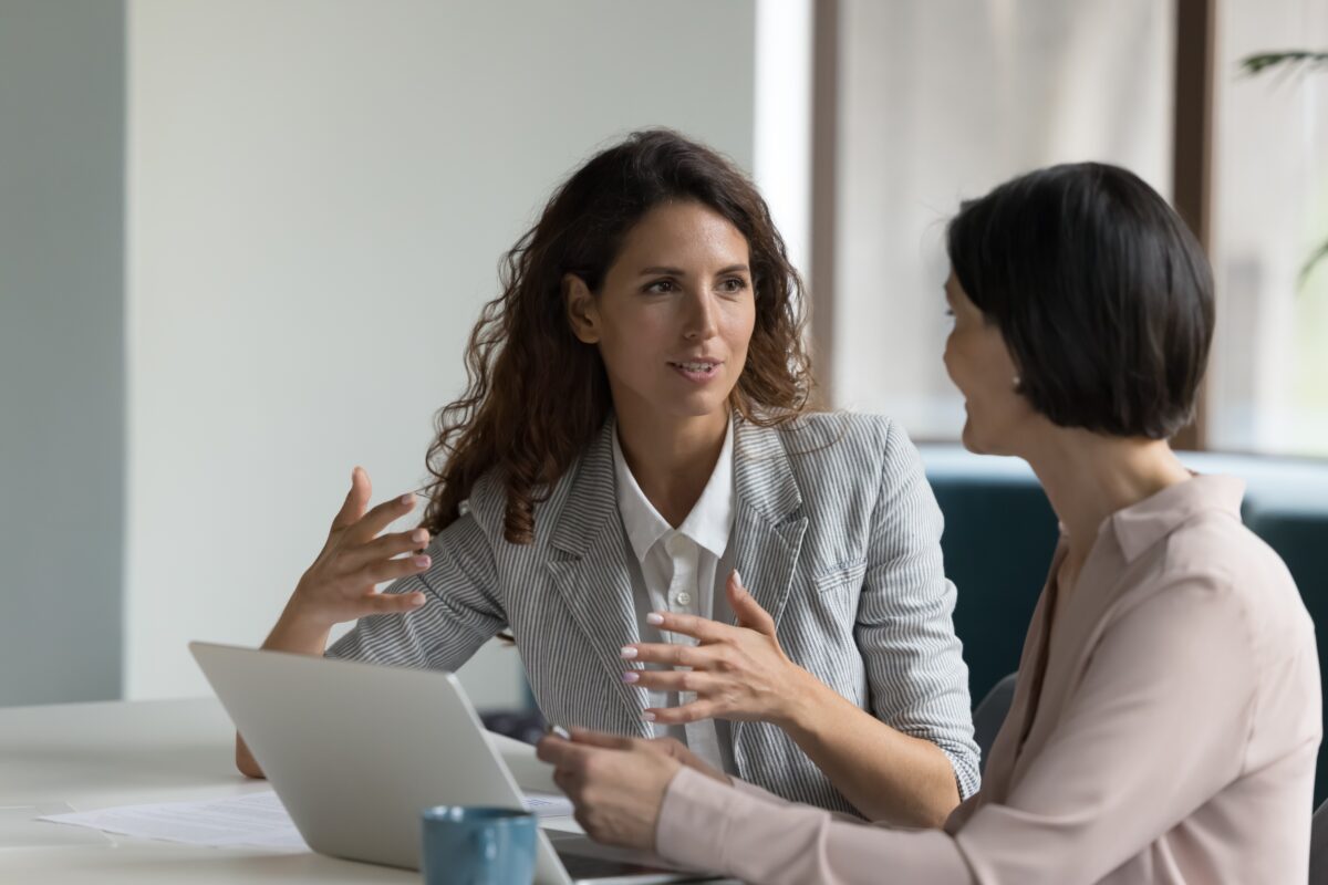 two women in discussion at a conference table one talking with her hands