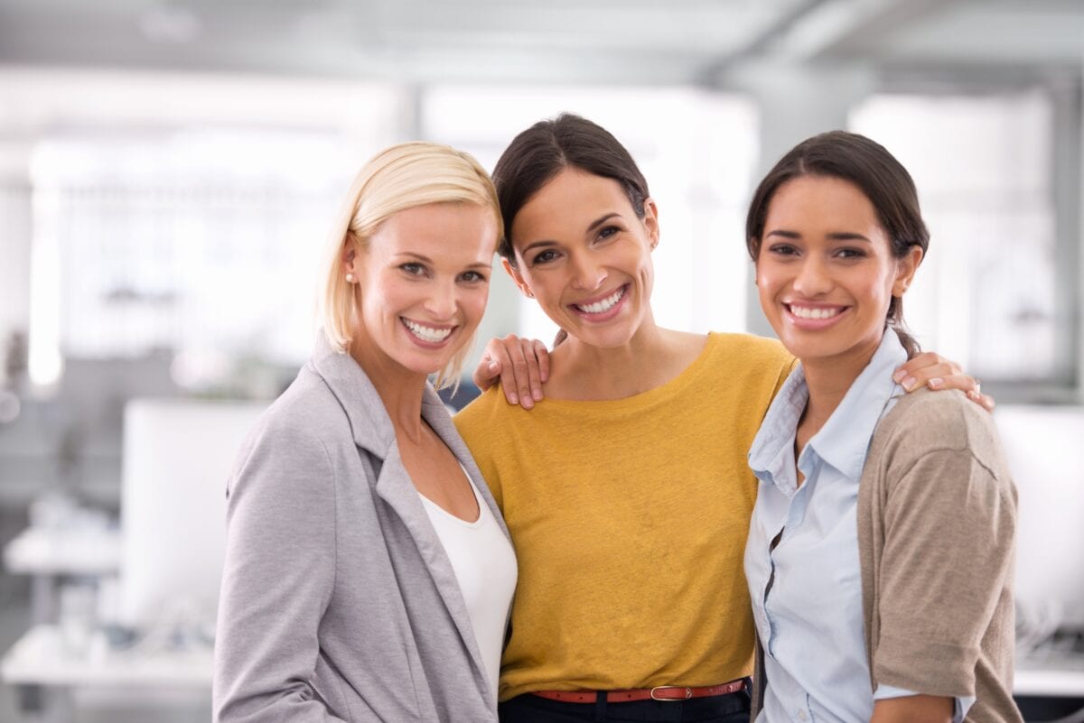 Three coworkers posing together and smiling in an office workspace