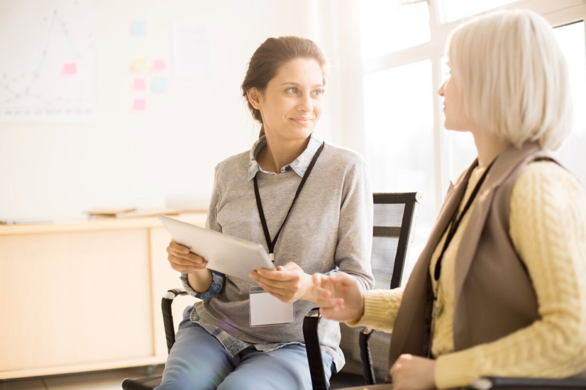 Two women wearing badges talking during a coaching conversation while reviewing a tablet
