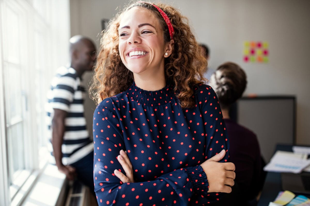 Smiling professional standing with arms crossed in a collaborative office workspace