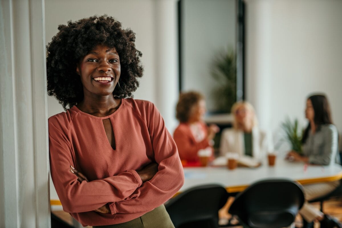 Confident professional standing with arms crossed in front of colleagues meeting in a modern office