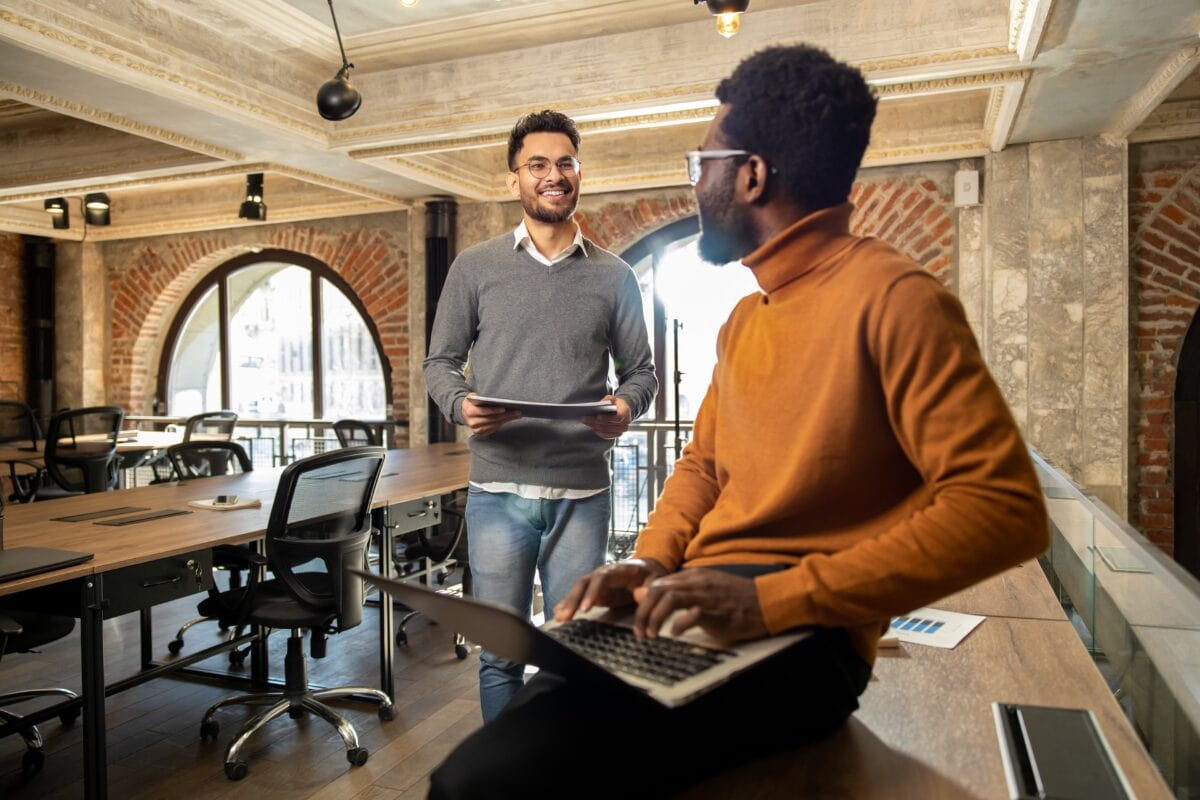Two coach educators working together in a shared office space with laptops and documents.