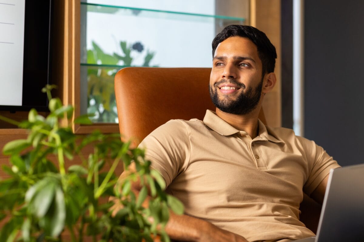 Man sitting in chair with laptop looking away thoughtfully in office