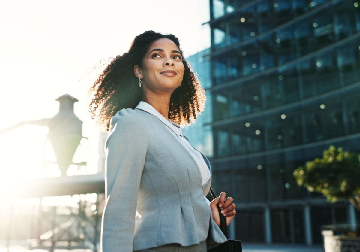 Businesswoman walking outdoors in a city environment, appearing thoughtful and confident as she moves forward.