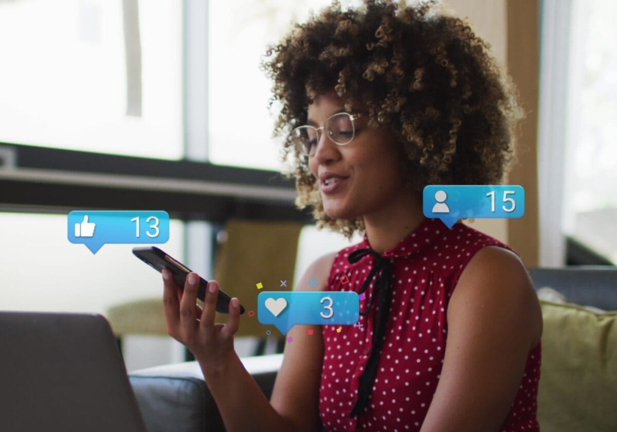  A smiling professional looking at a smartphone with floating social media icons for likes, follows, and hearts.