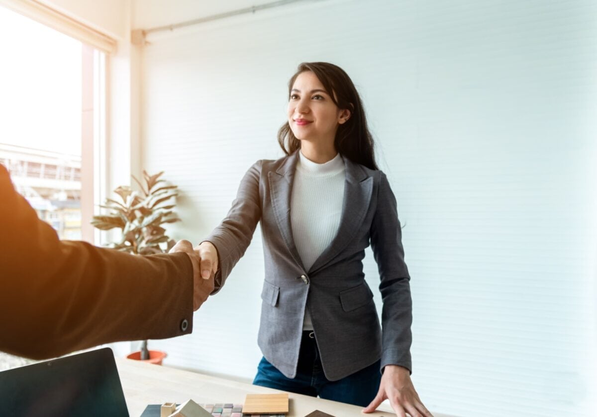 A confident professional woman shaking hands across a desk in a bright office, representing trust and boundary-setting in a coaching relationship.