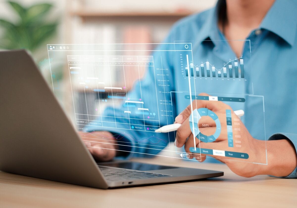 A person using a stylus to interact with a digital project management dashboard hovering over a laptop.