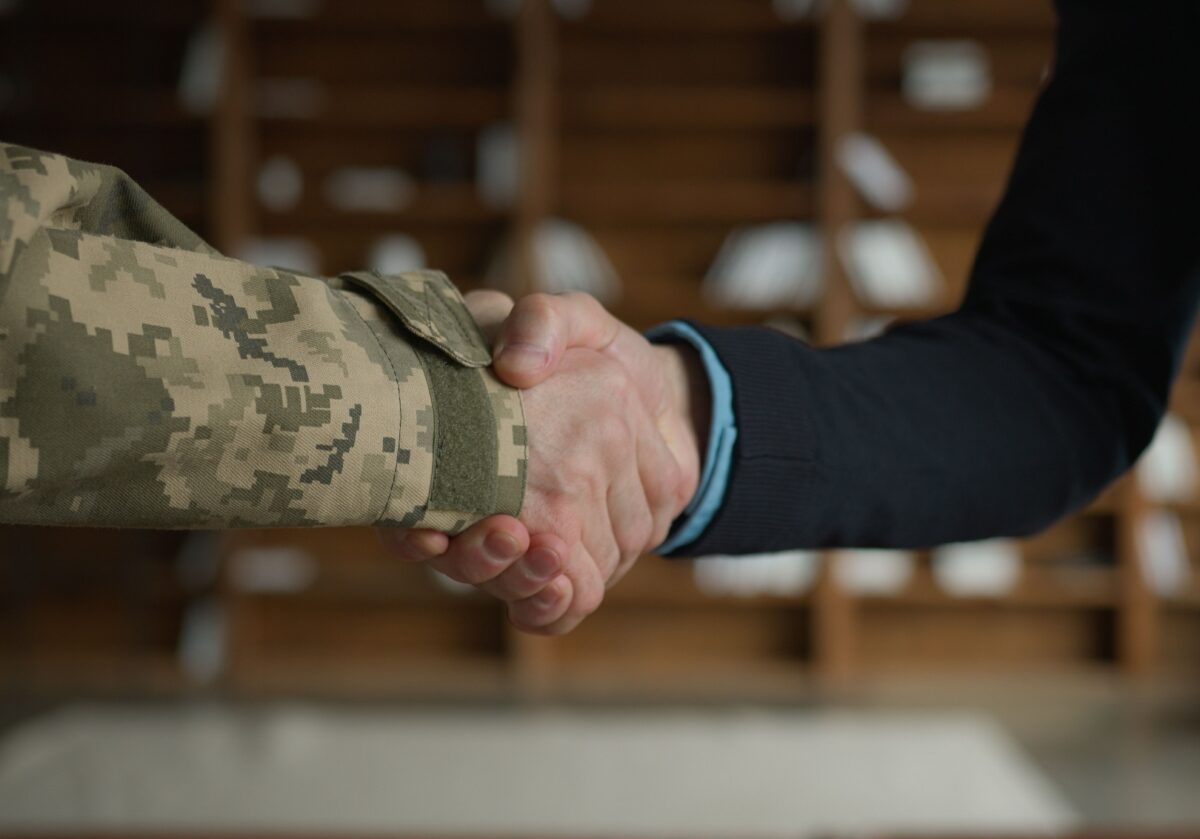 A military service member in a camouflage uniform shakes hands with a civilian, symbolizing a veteran's transition to a coaching career.