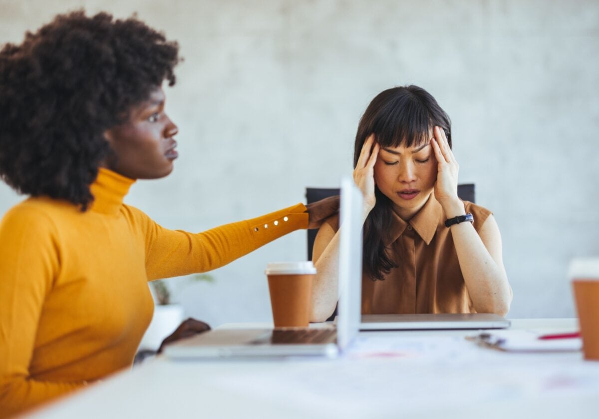 Woman comforting stressed peer at desk during a challenging coaching moment.