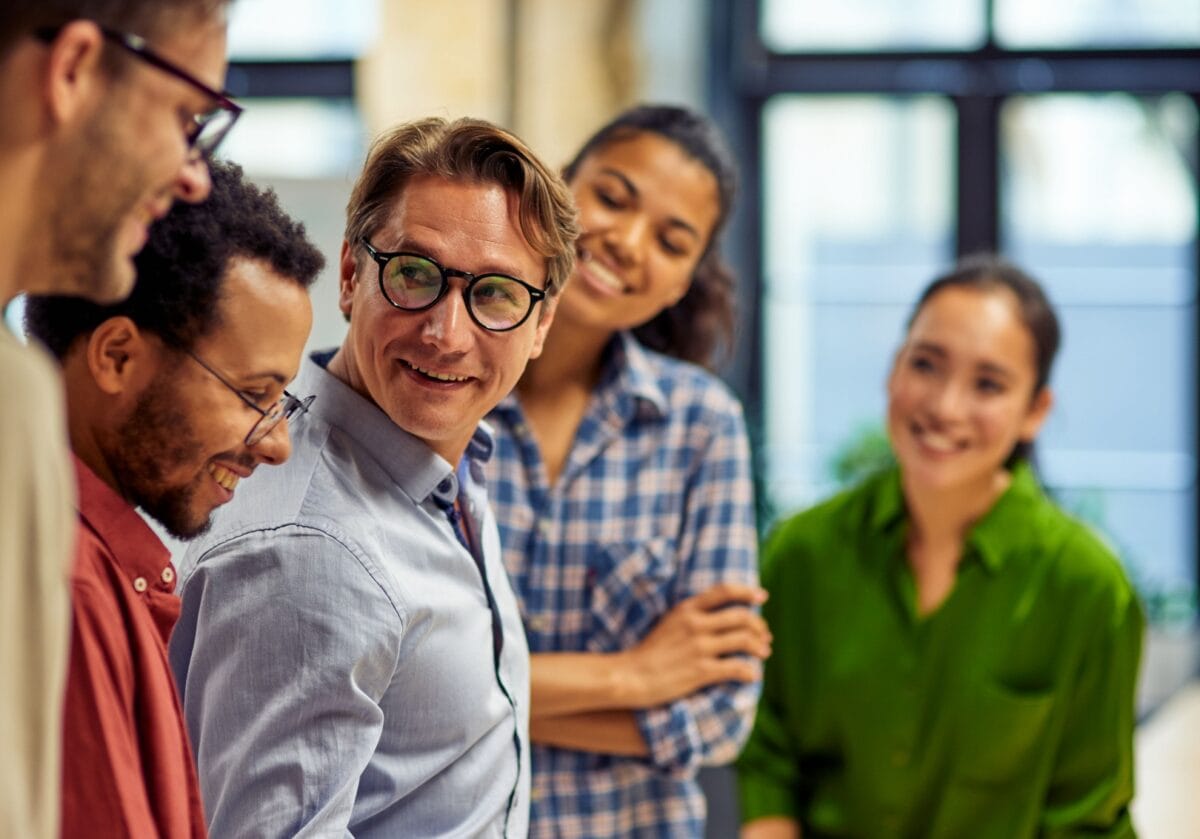 A diverse group of professionals collaborating in a workplace discussion, demonstrating leadership engagement and the positive impact of leadership coaching.