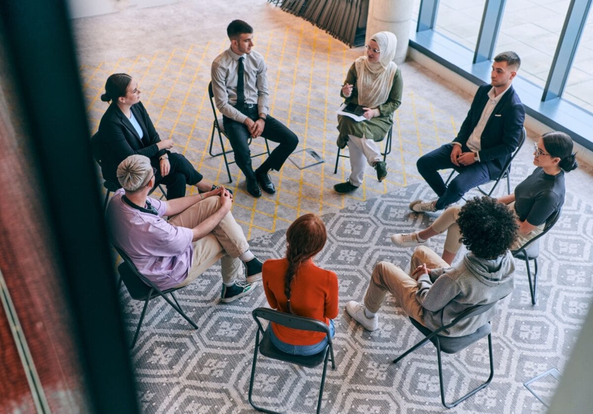 Diverse group of coaches gathered in a circle, discussing belonging through service
