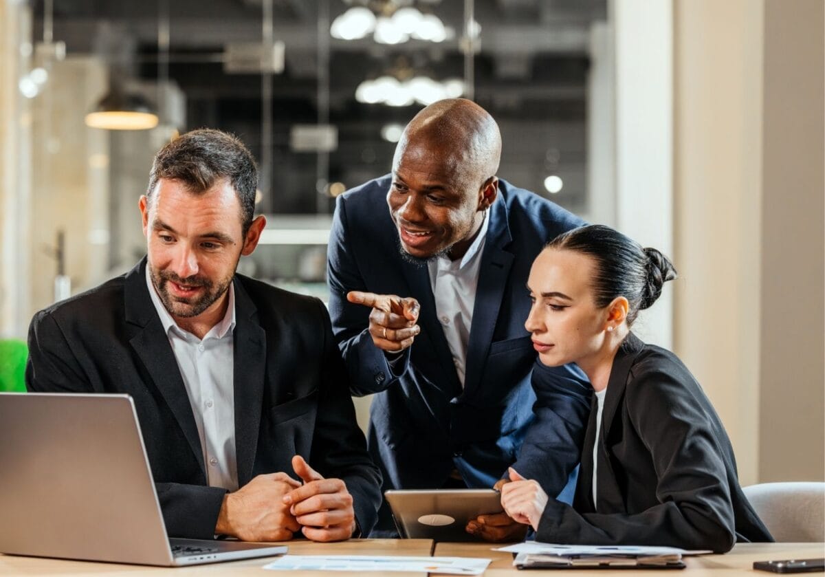 Three business professionals collaborating around a laptop and discussing a project in an office.