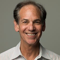 Larry Ackerman ACC headshot photo, smiling man with gray hair and light collared top in front of gray background