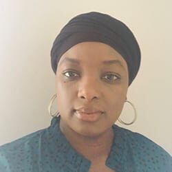 Coura Badiane MBA CAE headshot photo, smiling woman with dark shirt on and hoop earrings